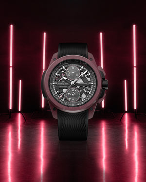Luxury watch with black strap and detailed face on a reflective surface with red neon lights in the background