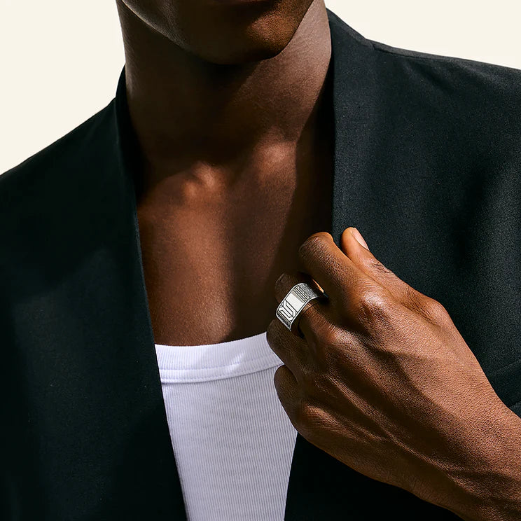 Person wearing a black blazer over a white shirt, with a close-up of a ring.