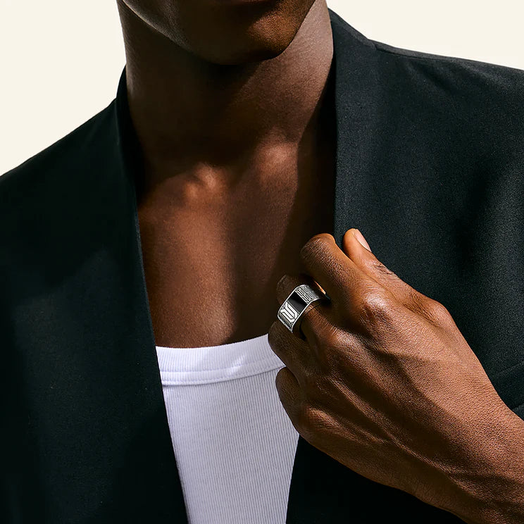 Person wearing a black blazer and white shirt, adjusting a silver ring on their finger.
