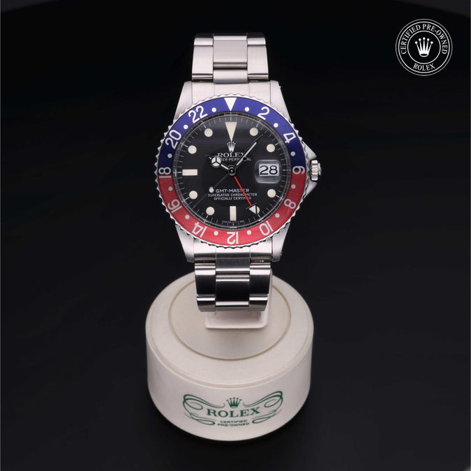 Rolex watch with a black, red, and blue face on a white stand against a dark background