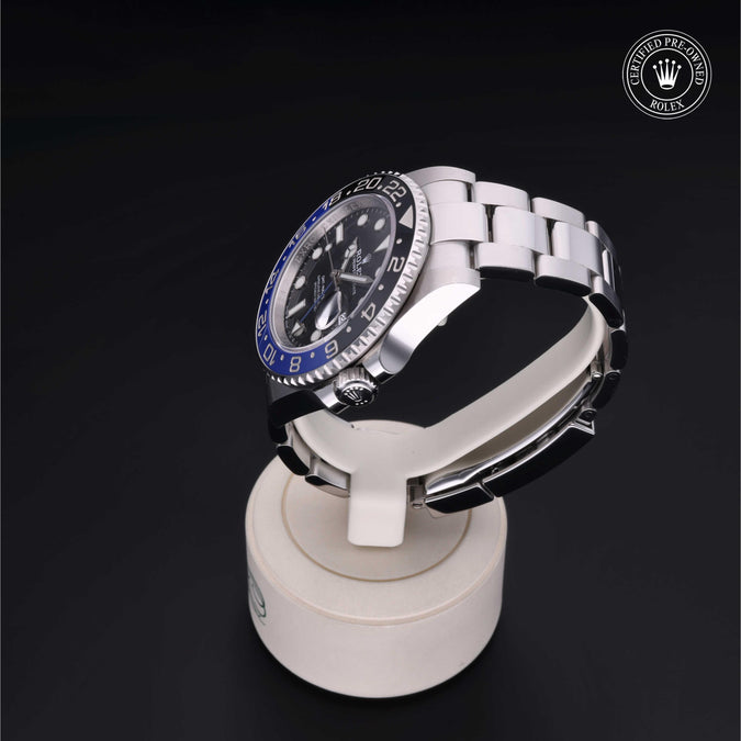 Three-quarter view of Rolex GMT-Master II 40 mm steel watch showing black dial and blue-and-black 24-hour bezel on a white display stand, Rolex Certified Pre-Owned seal visible