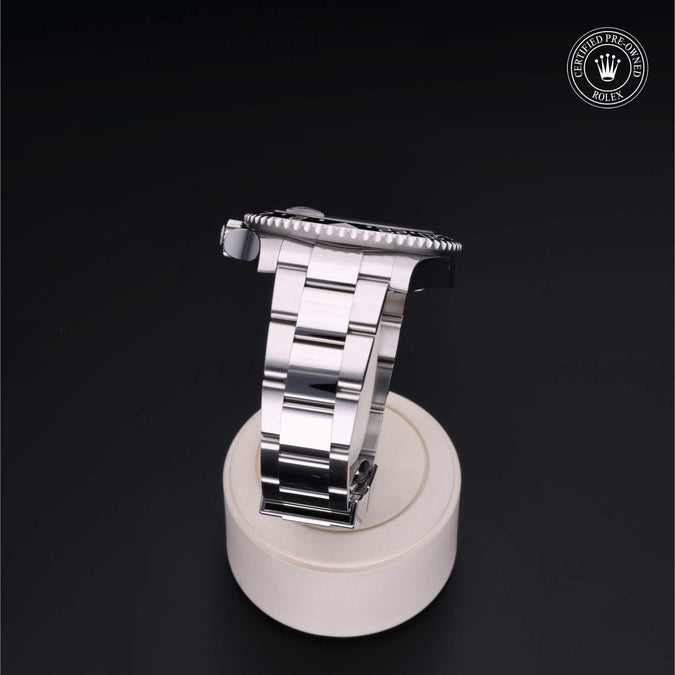 Side view of Rolex GMT-Master II showing polished stainless steel Oyster bracelet on a white display stand against a dark background