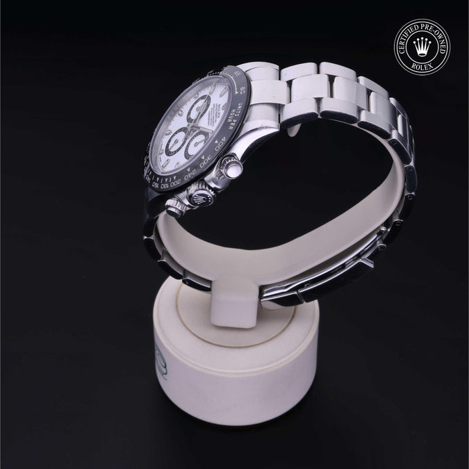 Three-quarter view of Rolex Cosmograph Daytona, steel with white dial and black bezel, on white stand with Certified Pre-Owned seal