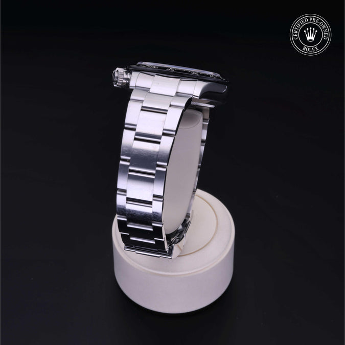 Side view of Rolex Cosmograph Daytona showing stainless steel Oyster bracelet on white stand against black background