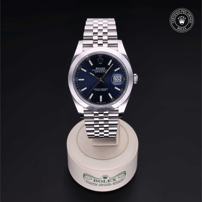 Front view of Rolex Datejust 41 watch showcasing blue dial, date window and jubilee bracelet on white stand against black background