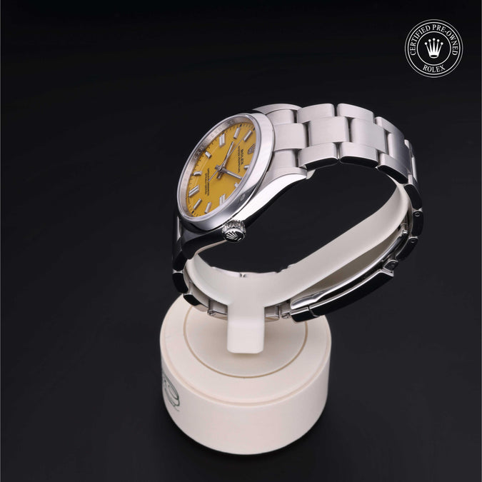 Silver watch with yellow face on a white stand against a black background, featuring a Rolex logo.