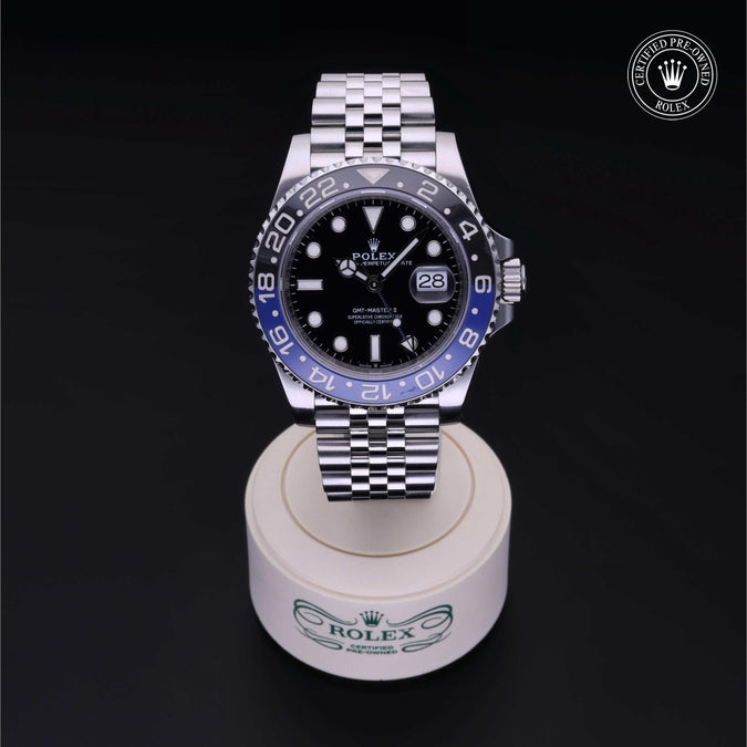 Rolex with black dial and steel bracelet on a white stand with a black background.