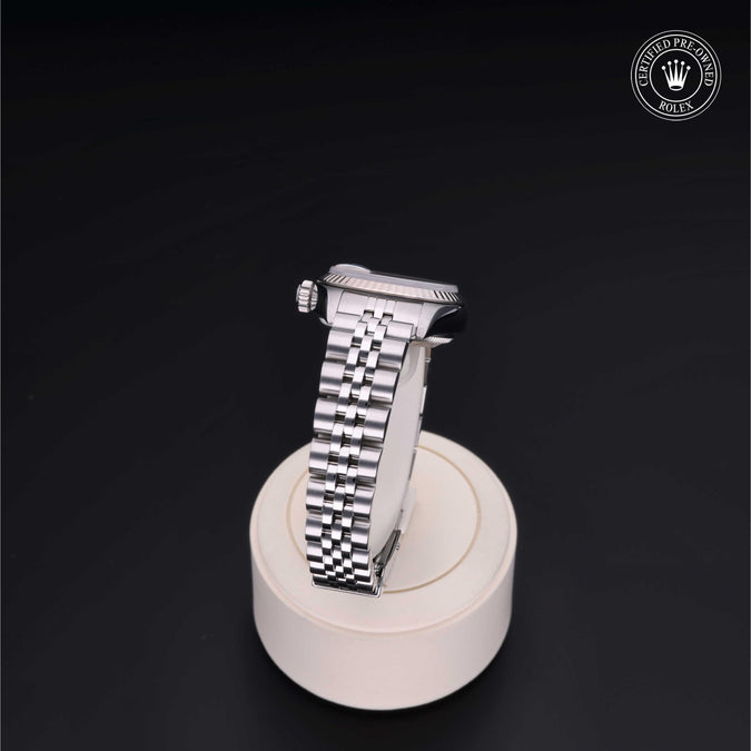 Silver watch on a white stand with a dark background