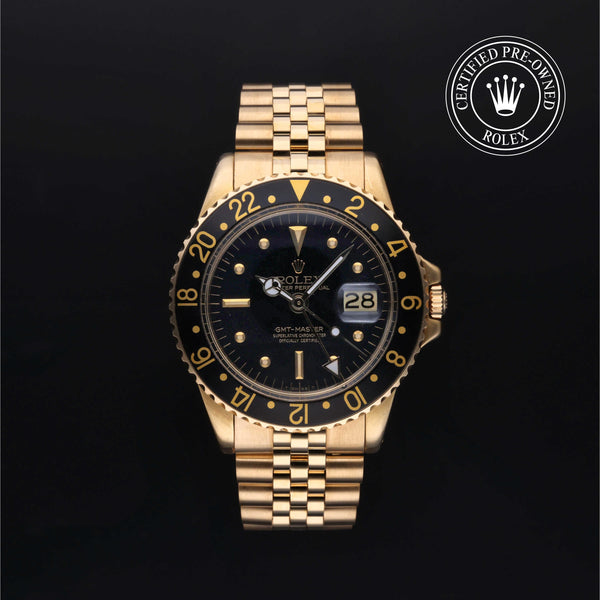 A gold-tone Rolex GMT-master watch with a black dial and black bezel featuring gold markings, shown against a black background with a 'Certified Pre-Owned Rolex' emblem in the top right corner.