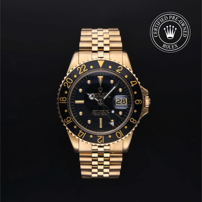A gold-tone Rolex GMT-master watch with a black dial and black bezel featuring gold markings, shown against a black background with a 'Certified Pre-Owned Rolex' emblem in the top right corner.
