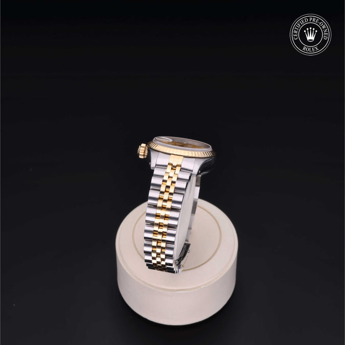 Two-tone watch on a white stand with a dark background