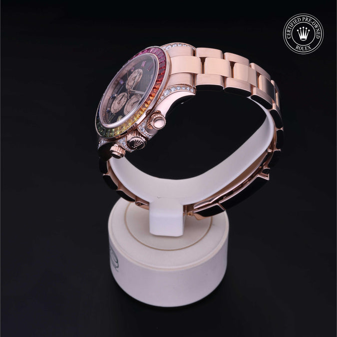 A luxury watch with a rose gold metal bracelet and a bezel featuring a rainbow color-streak design, displayed on a white stand against a black background.