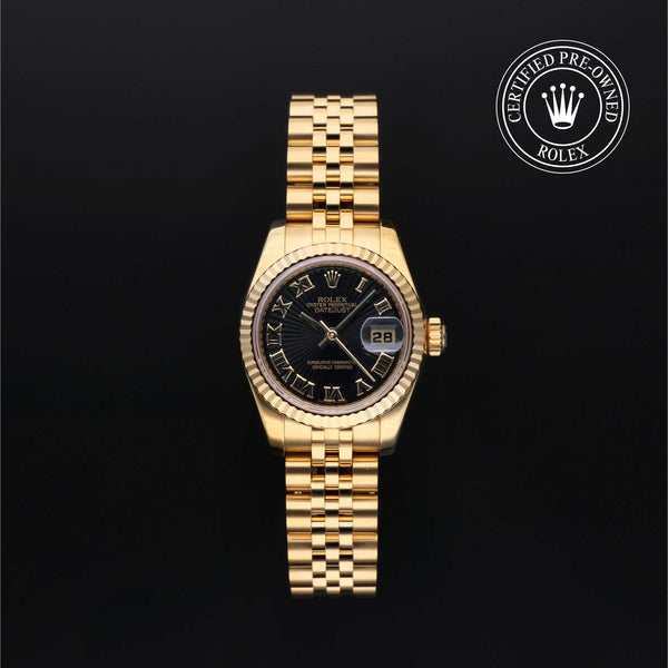 A gold-tone Rolex Datejust watch with a black sunburst dial, Roman numeral hour markers, and a fluted bezel, displayed on a black background with a 'Certified Pre-Owned Rolex' emblem in the top right corner.