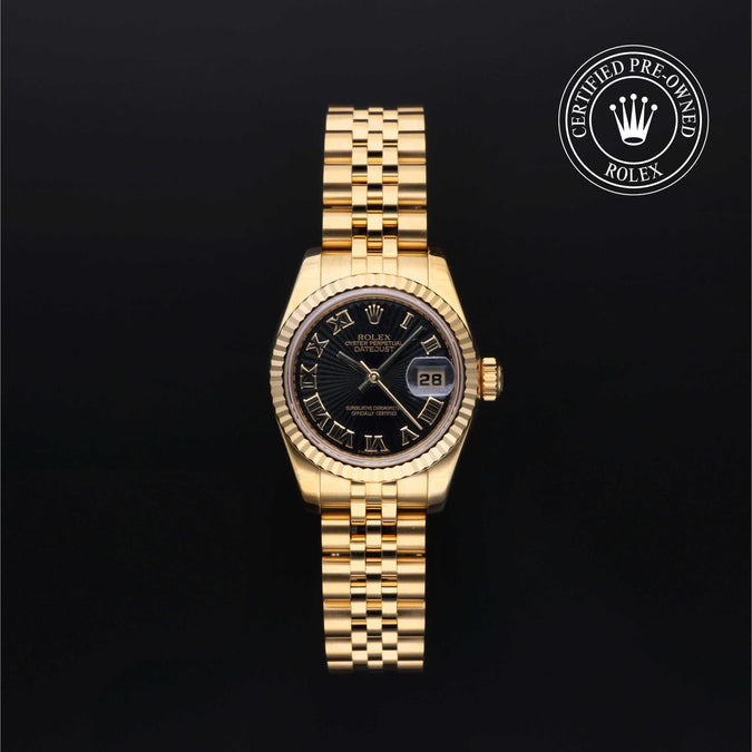 A gold-tone Rolex Datejust watch with a black sunburst dial, Roman numeral hour markers, and a fluted bezel, displayed on a black background with a 'Certified Pre-Owned Rolex' emblem in the top right corner.