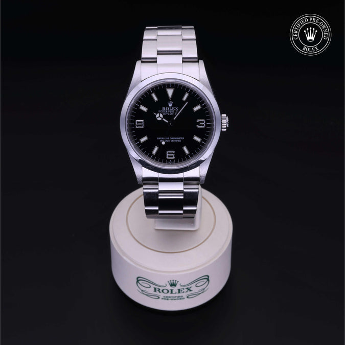 Silver Rolex with back dial sitting on a white stand with branded logo on a black background