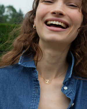 a woman laughing outside with denim shirt wearing a gold necklace