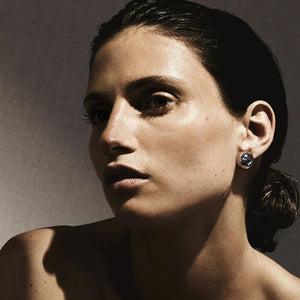 Close-up of model wearing Pinball stud earrings in 925 silver, hand-hammered spherical design on neutral background