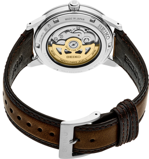 Rear view of a Seiko watch with a silver stainless steel case and a brown leather strap, showing the gold-toned mechanical movement through a transparent back.