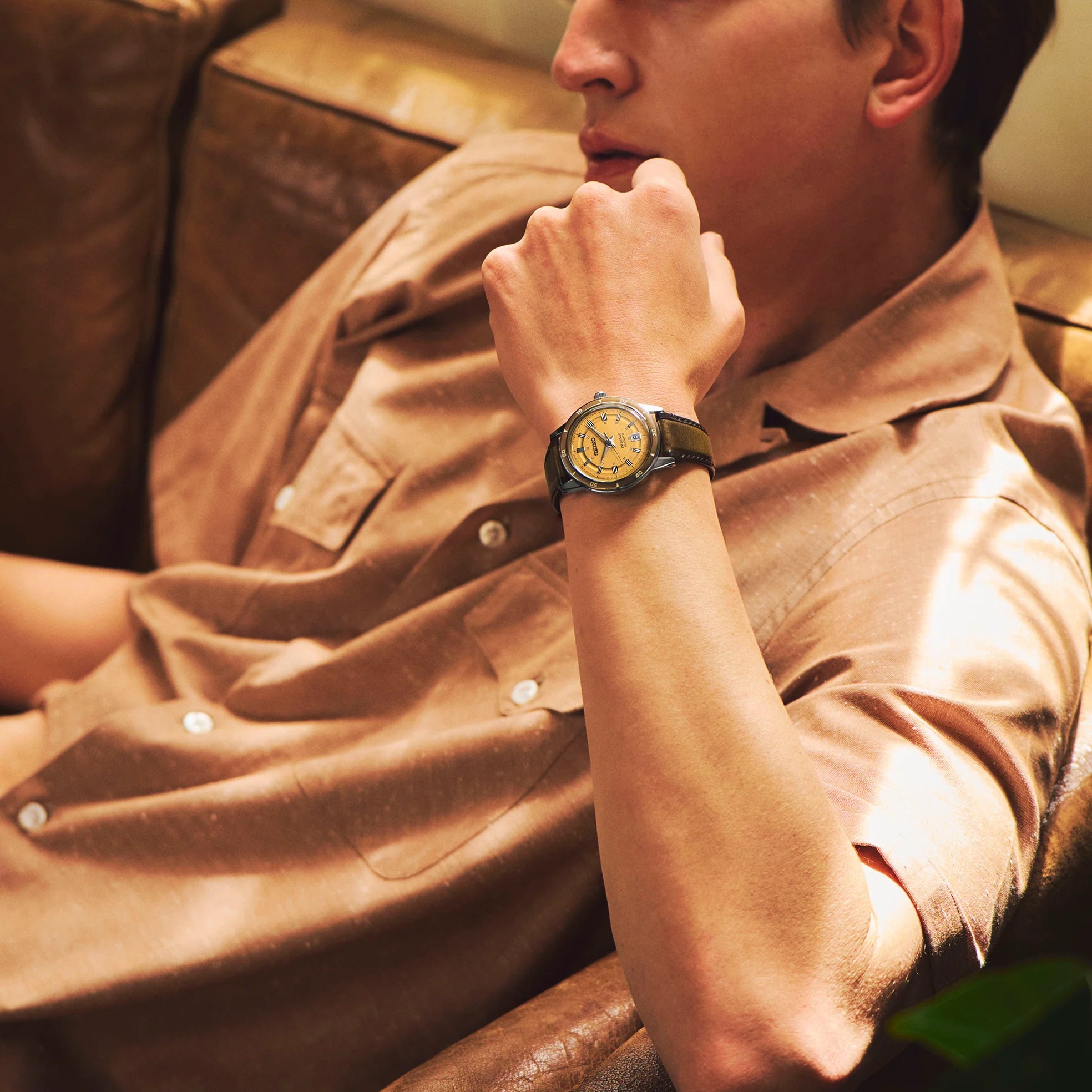 Man wearing a watch with a brown leather jacket sitting on a couch.