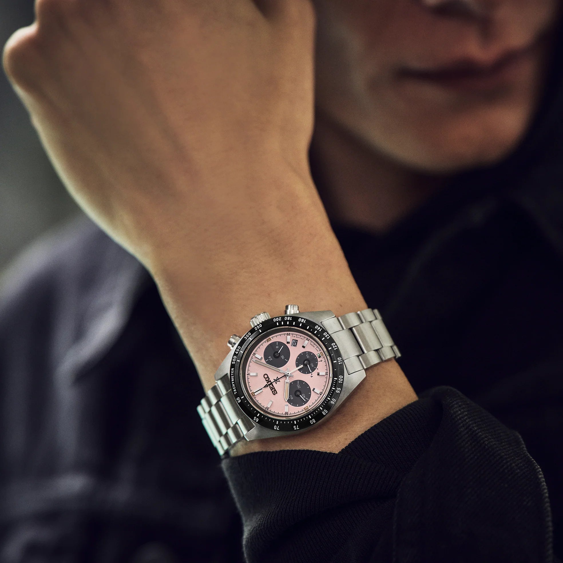 Close-up of a person wearing a silver watch with a pink face.