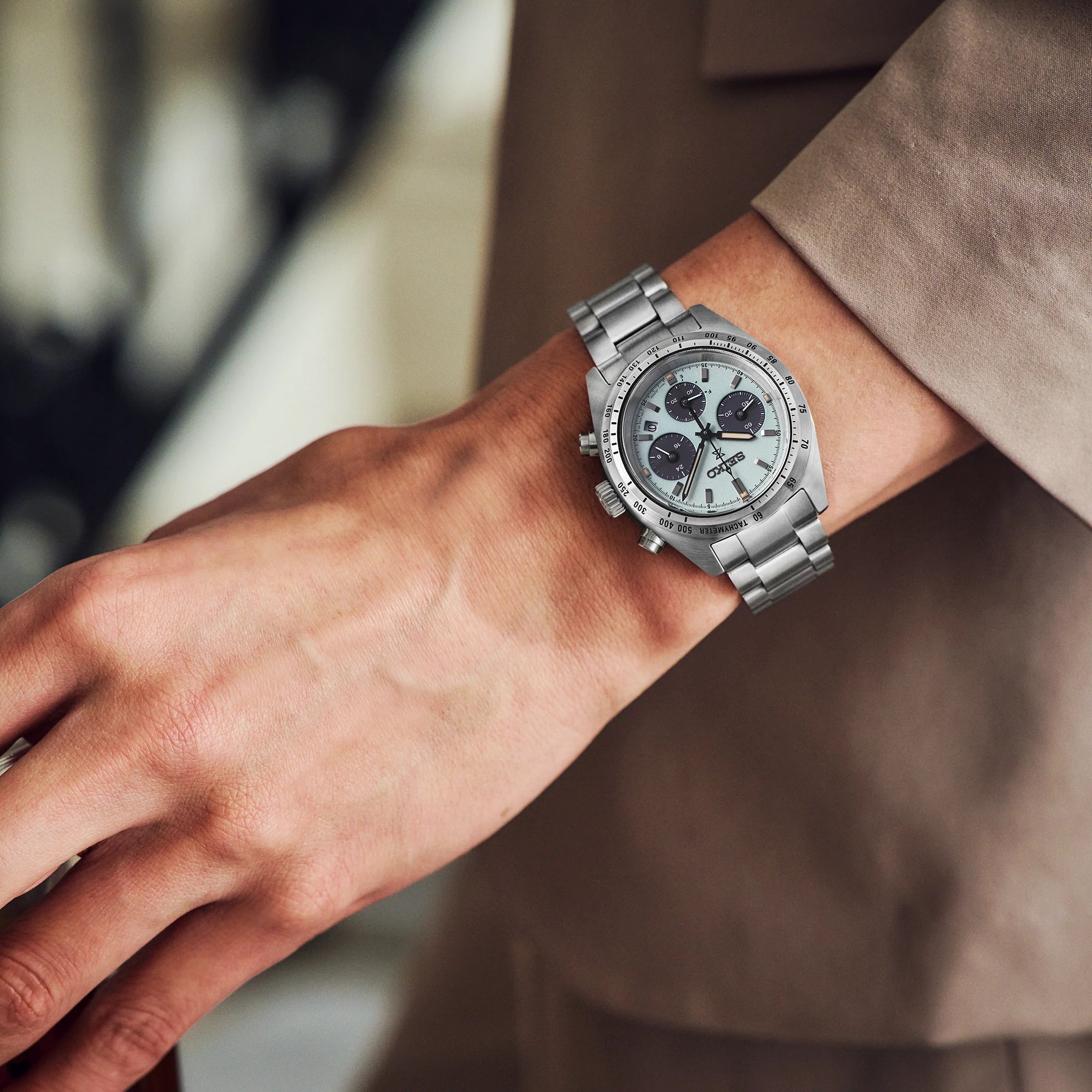 Close up of a silver watch on a man's wrist wearing a beige jacket 