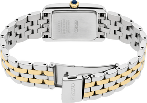 The back view of a Seiko women's watch featuring a two-tone stainless steel and yellow gold link bracelet with a silver-toned rectangular case and a blue cabochon crown.