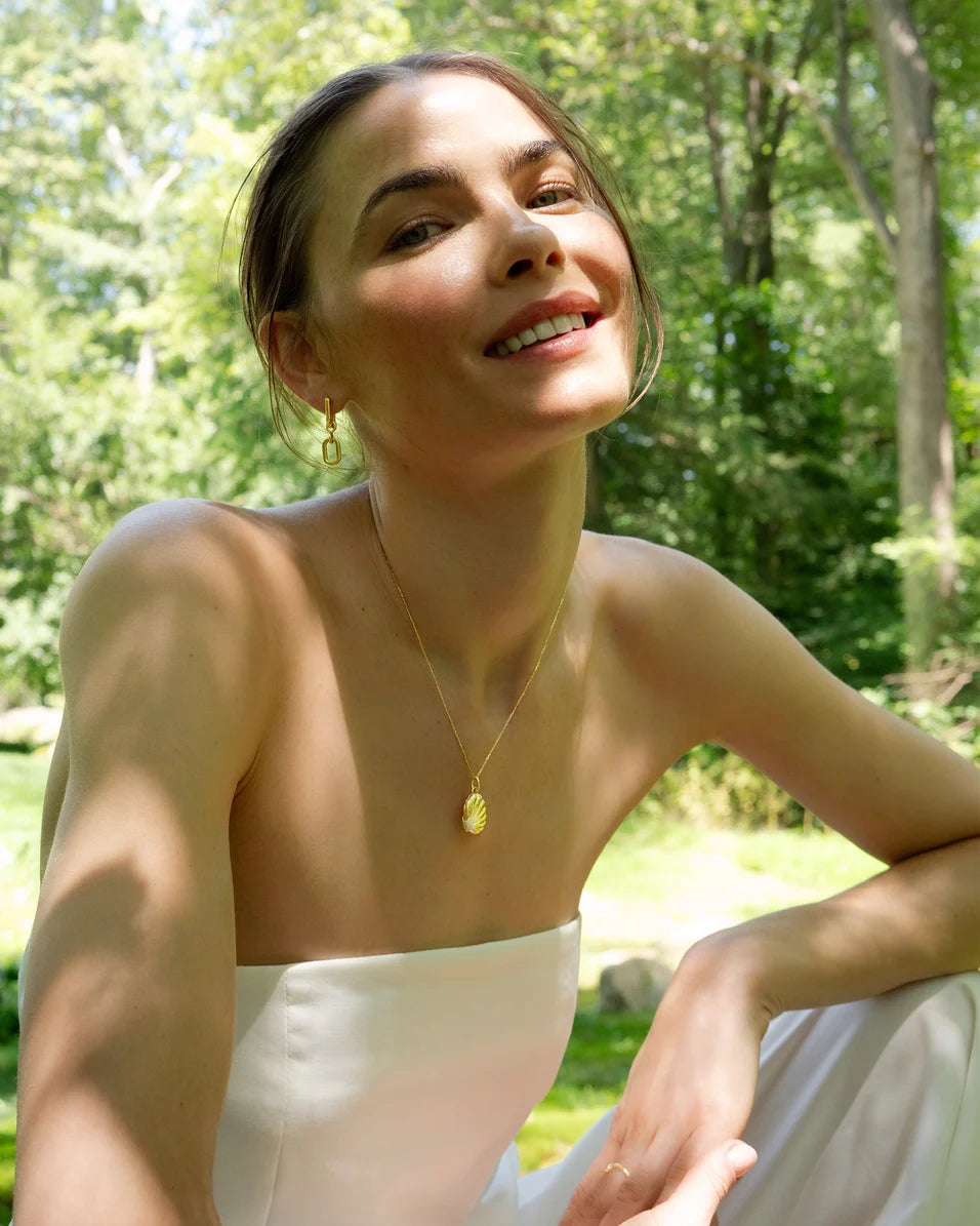 a woman sitting outside with a gold necklace and white dress