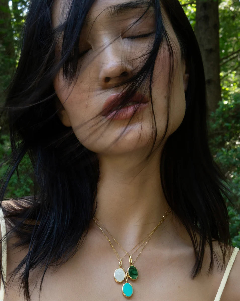 woman standing outside hair in face wearing gold necklaces