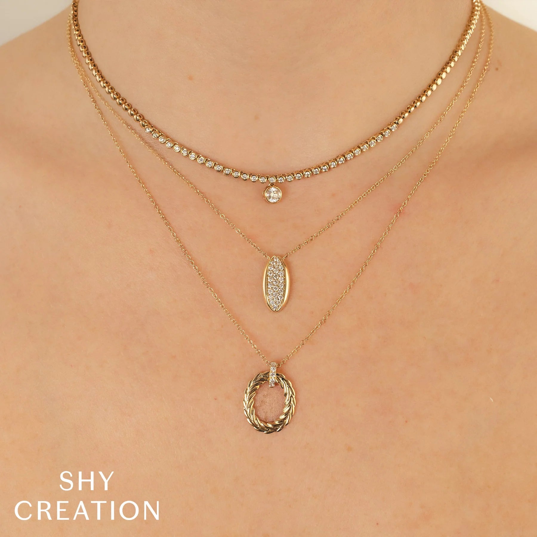 Three layered gold necklaces with oval diamond pendant and braided circular pendant; SHY CREATION