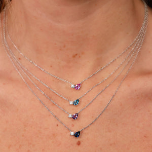 Four-layer silver necklaces on a neck, each with a small round diamond and teardrop gemstone in pink, teal, purple, navy