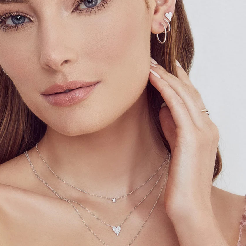 Model close-up wearing layered white gold necklaces, including a diamond pavé heart pendant and a bezel pendant