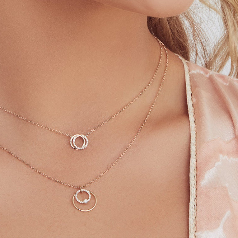 Two-layer rose-gold necklace set with two circle pendants worn on a woman's neck and collarbone.