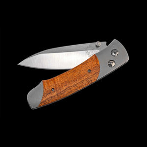 A folding pocket knife with a satin-finished steel blade and a dual-tone wooden handle, shown open against a solid black background.