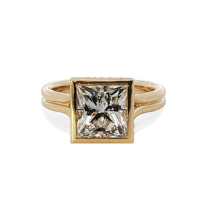 Front view of princess-cut diamond engagement ring in 18K yellow gold bezel setting on white background