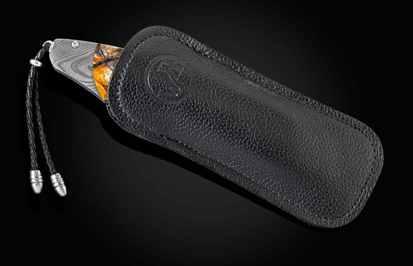 A folding pocket knife partially pulled from a black textured leather sheath with a braided cord lanyard, shown on a dark gradient background.