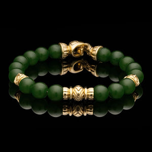 A beaded bracelet made of round dark green jade beads with polished gold-toned spacer beads and a gold-toned clasp, displayed on a reflective black surface.