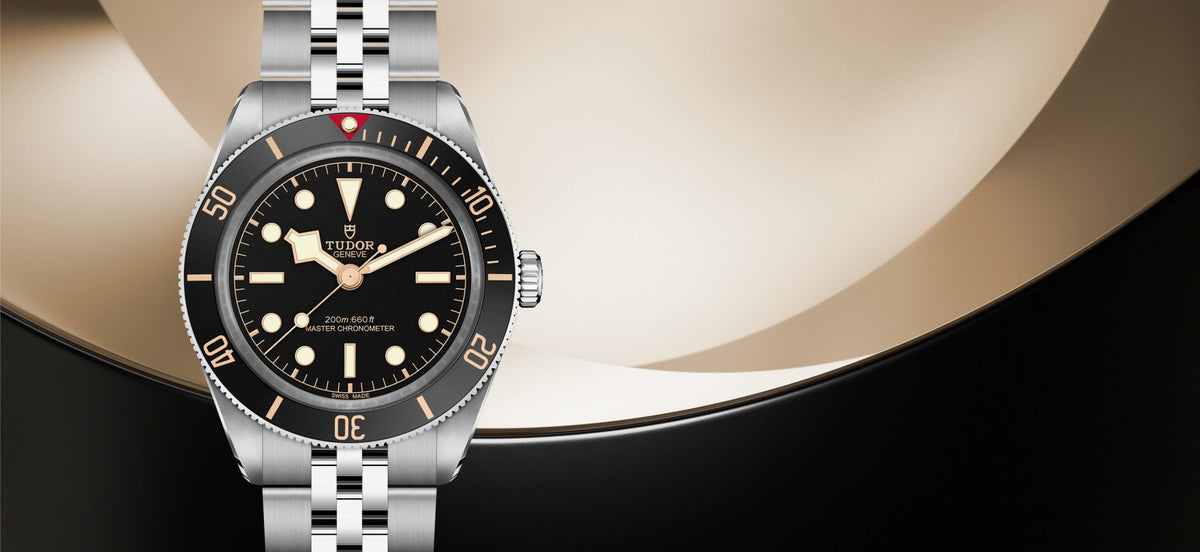Tudor silver watch with black dial and bezel with Tudor logo on a gold and black ground