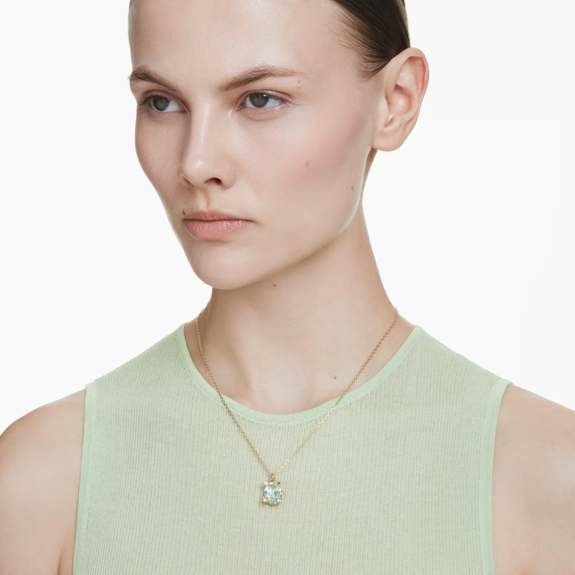 Neck view of Gema pendant with square green stone in gold-tone setting on delicate chain worn on model