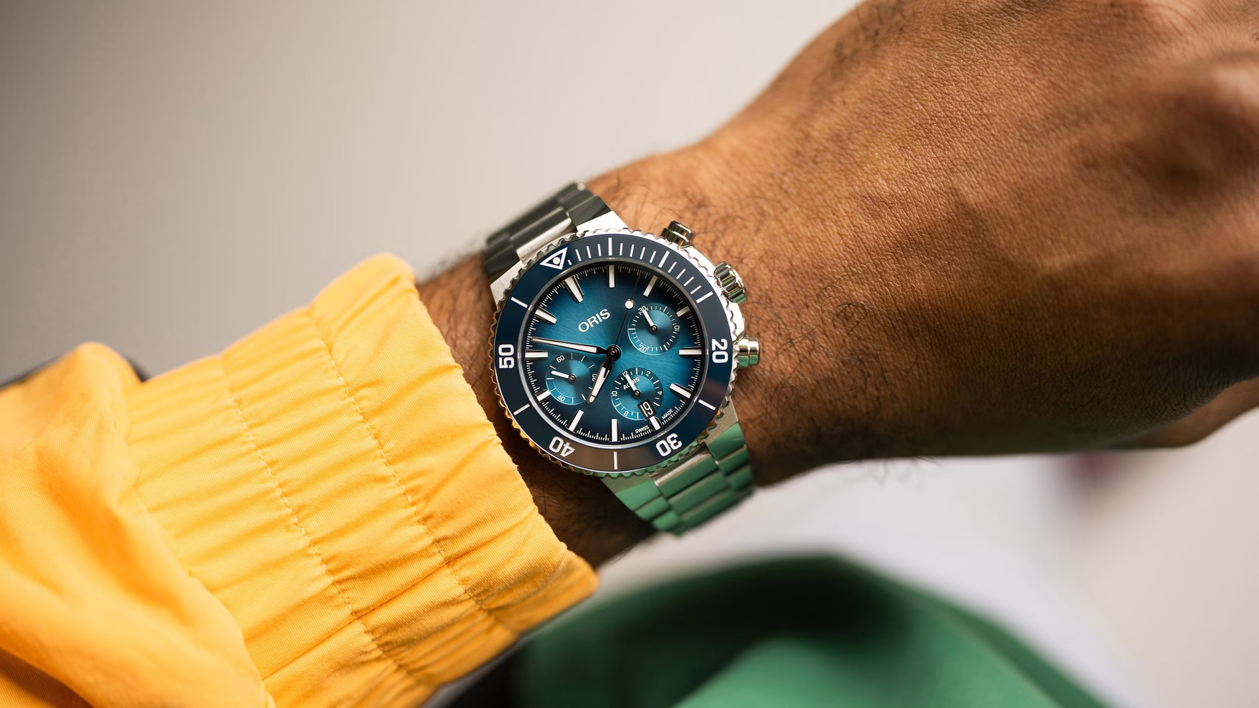 Close-up of a wrist wearing a watch with a blue face and stainless steel strap, against a neutral background.