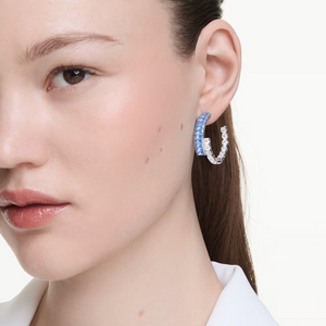 Close-up of model wearing Matrix Hoop Earrings with blue and clear crystals on two-tone hoop against white background