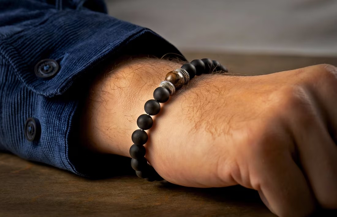 Black matte beaded men's bracelet with a tiger's eye bead and decorative silver spacers worn on a wrist