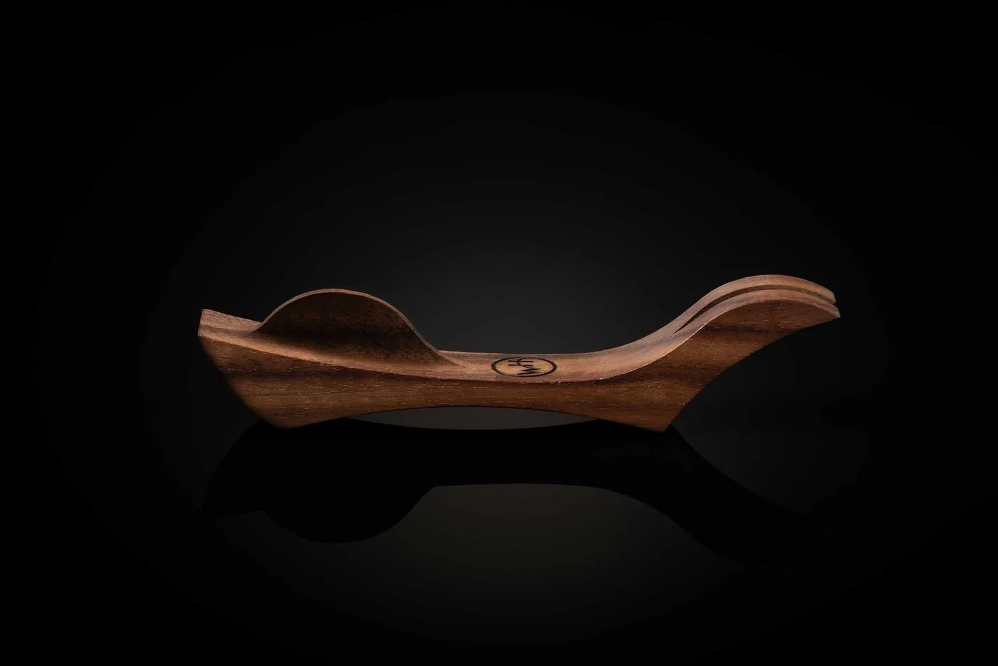 A curved wooden chair or lounge seat with a polished finish, shown from the side against a dark reflective background.
