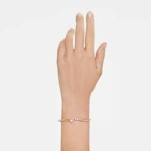 upclose of a hand and wrist wearing a gold tone open bangle with mixed cut stones on a white background