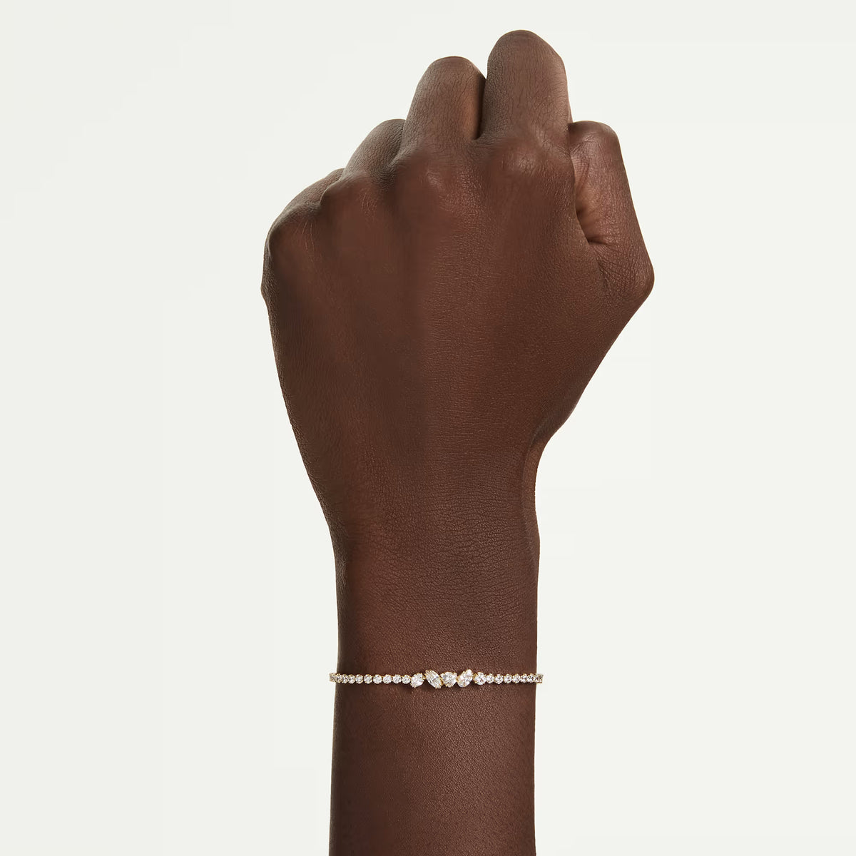 upclose of a hand and wrist wearing Gold tone bracelet with round and mixed cut stones on a white background