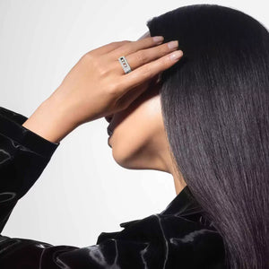 Person wearing a ring with a diamond, touching their hair against a neutral background