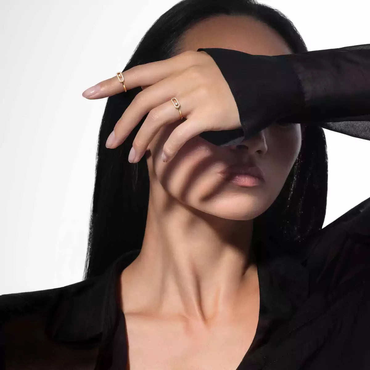 Person wearing a black shirt with a hand covering their face, wearing gold rings.