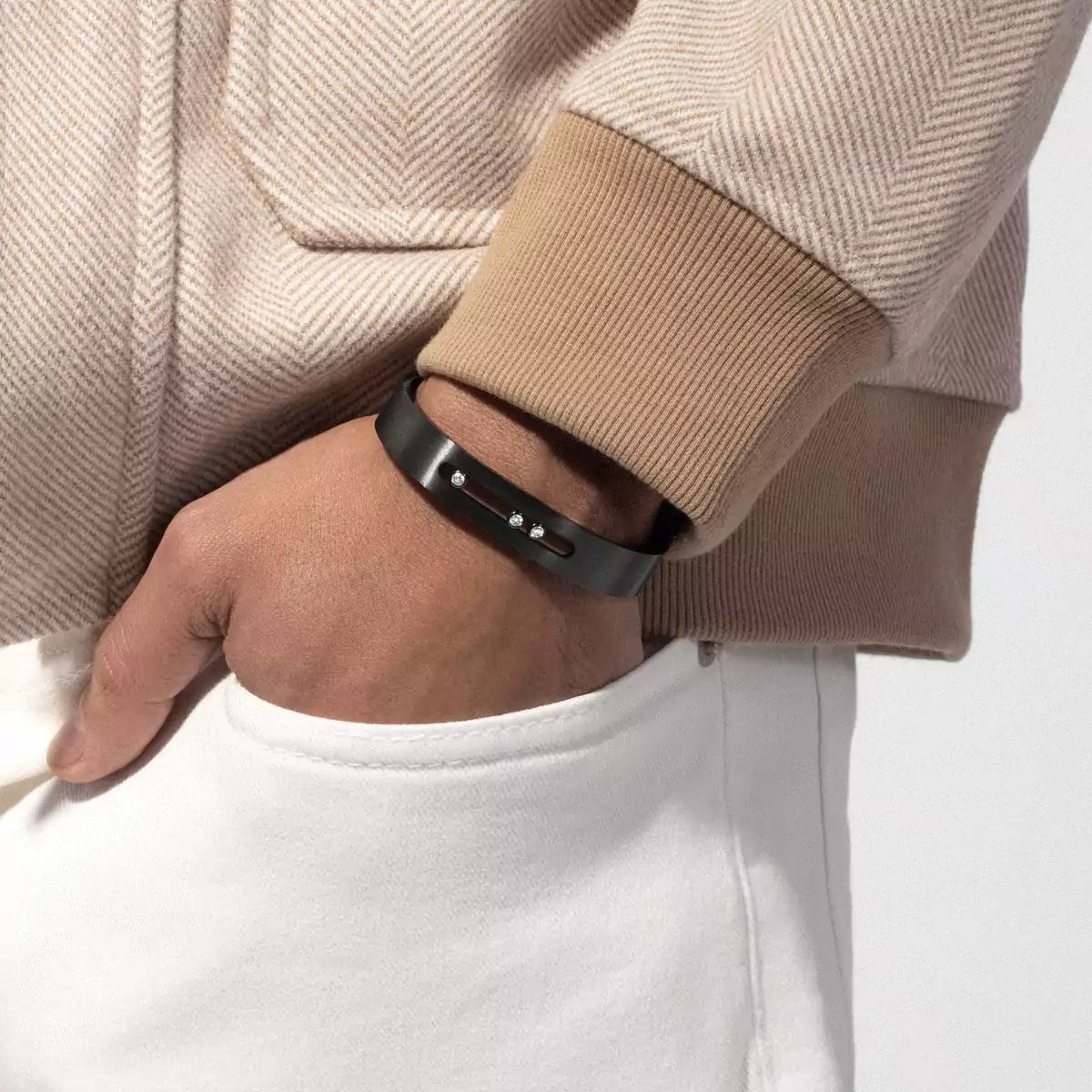 Close-up of wrist wearing Move Titanium graphite cuff bangle showcasing three moving brilliant cut diamonds with beige sleeve and white pocket background