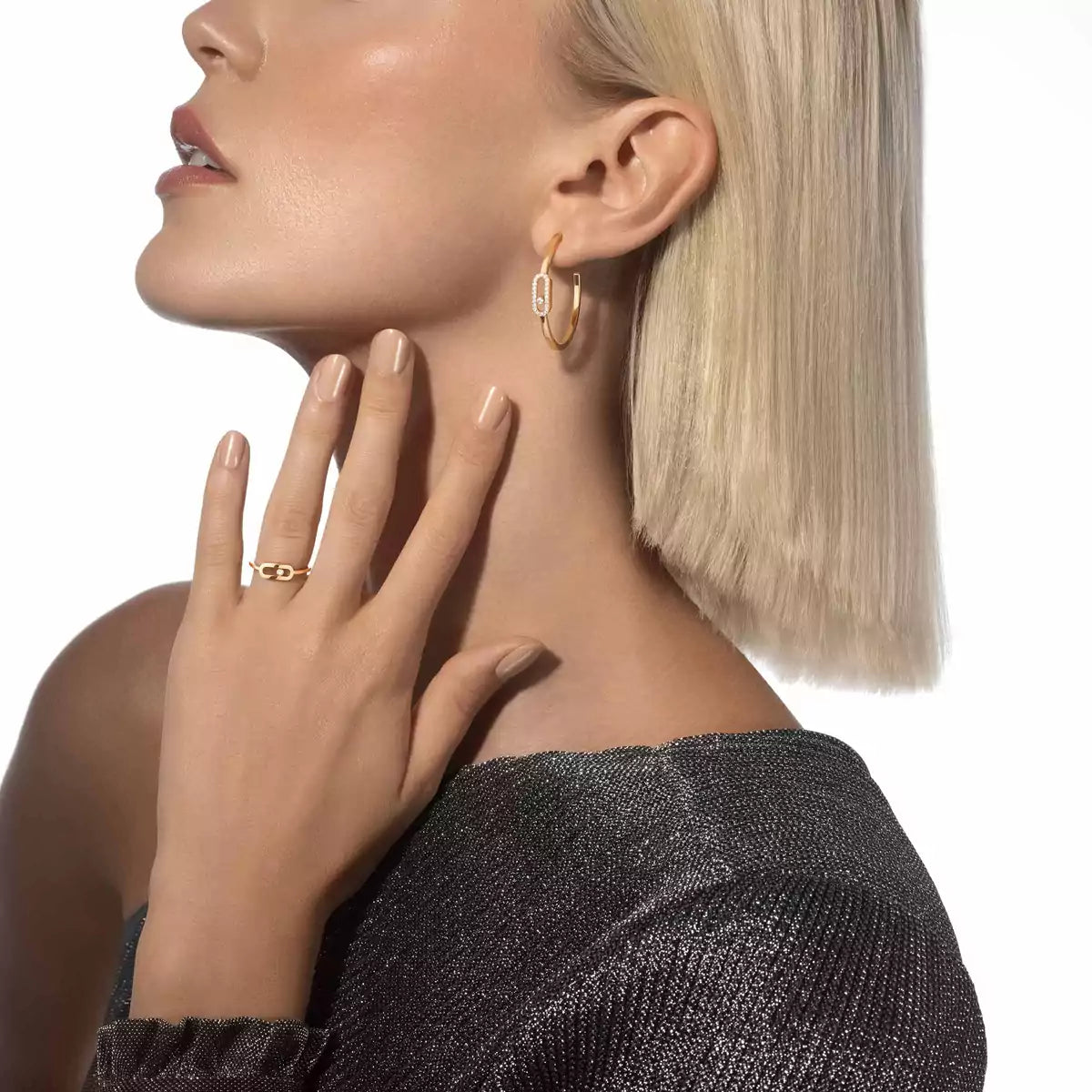 Close-up of a woman wearing gold hoop earrings and ring on a white background