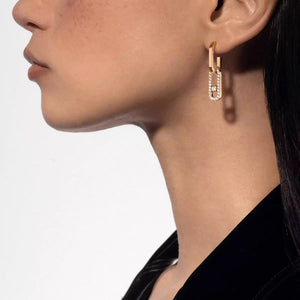 Close-up of a person wearing gold hoop earrings with small diamonds on a plain background