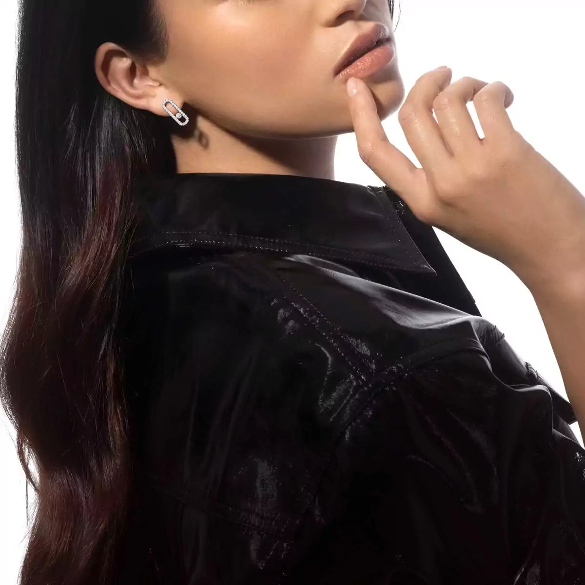 Woman wearing a black jacket and diamond earrings with a neutral background